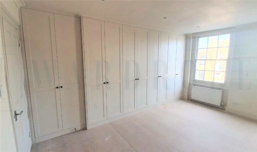 Bespoke white spray-painted Shaker style wardrobe in a bright room.