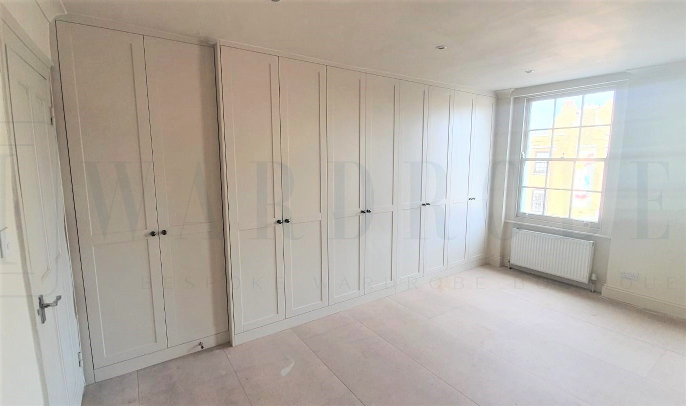 Bespoke white spray-painted Shaker style wardrobe in a bright room.