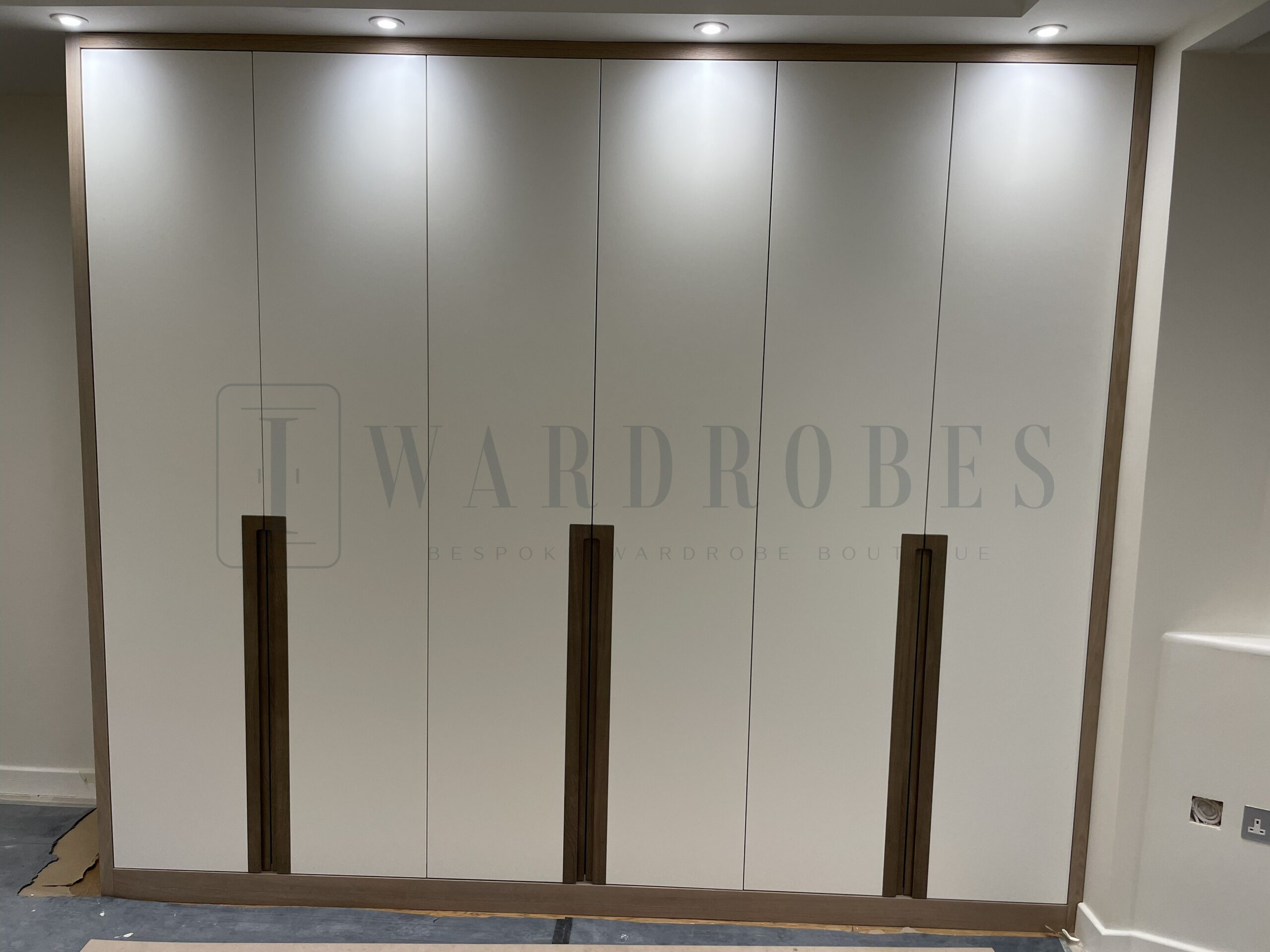 Modern white wardrobe with wooden handles in a contemporary bedroom.