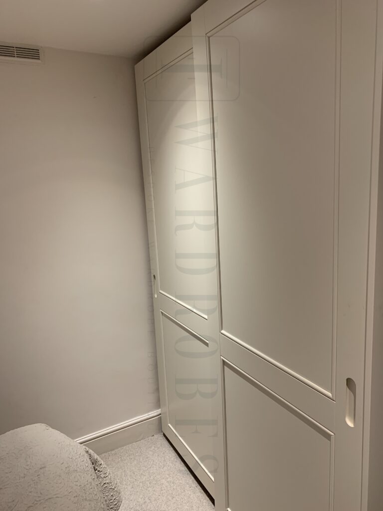 Modern white sliding door wardrobe with shaker style design in bedroom.