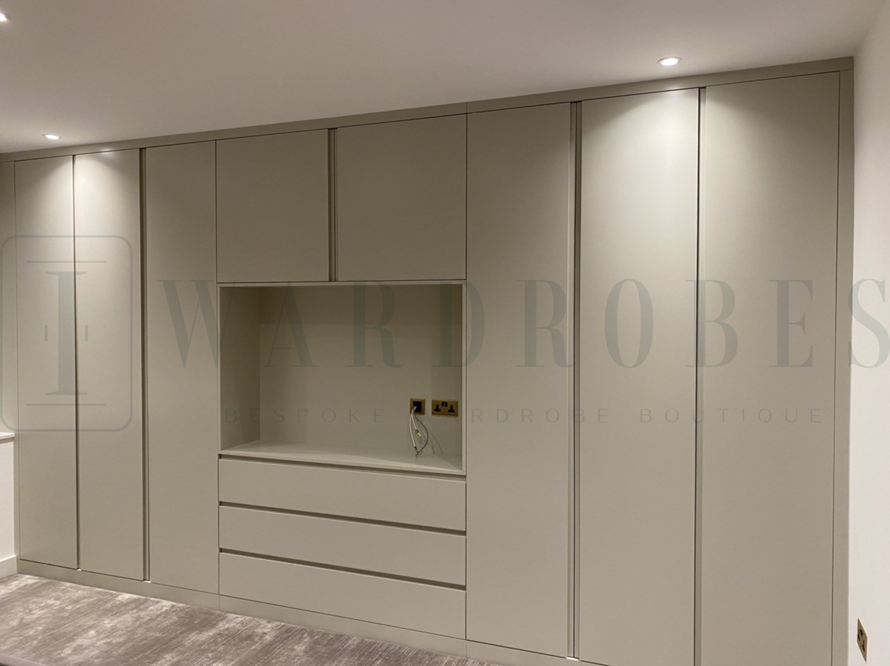Modern fitted wardrobe with routed handles and spray paint finish in a neutral colour.