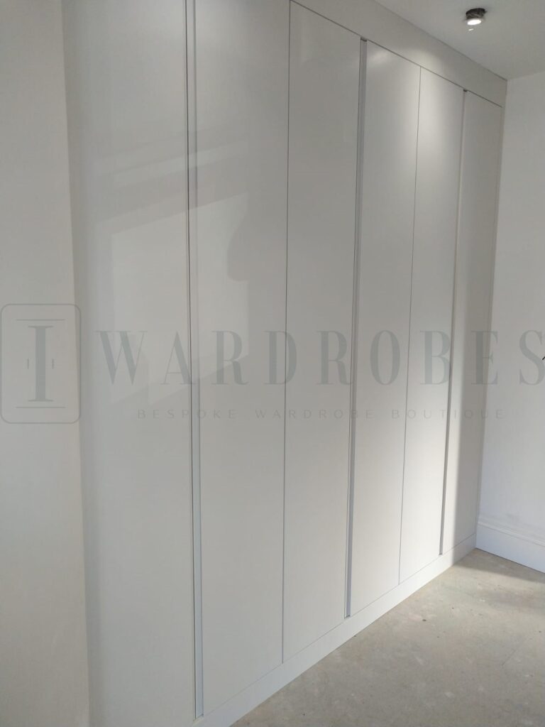 Modern white bespoke wardrobe with sloping ceiling design in bedroom.