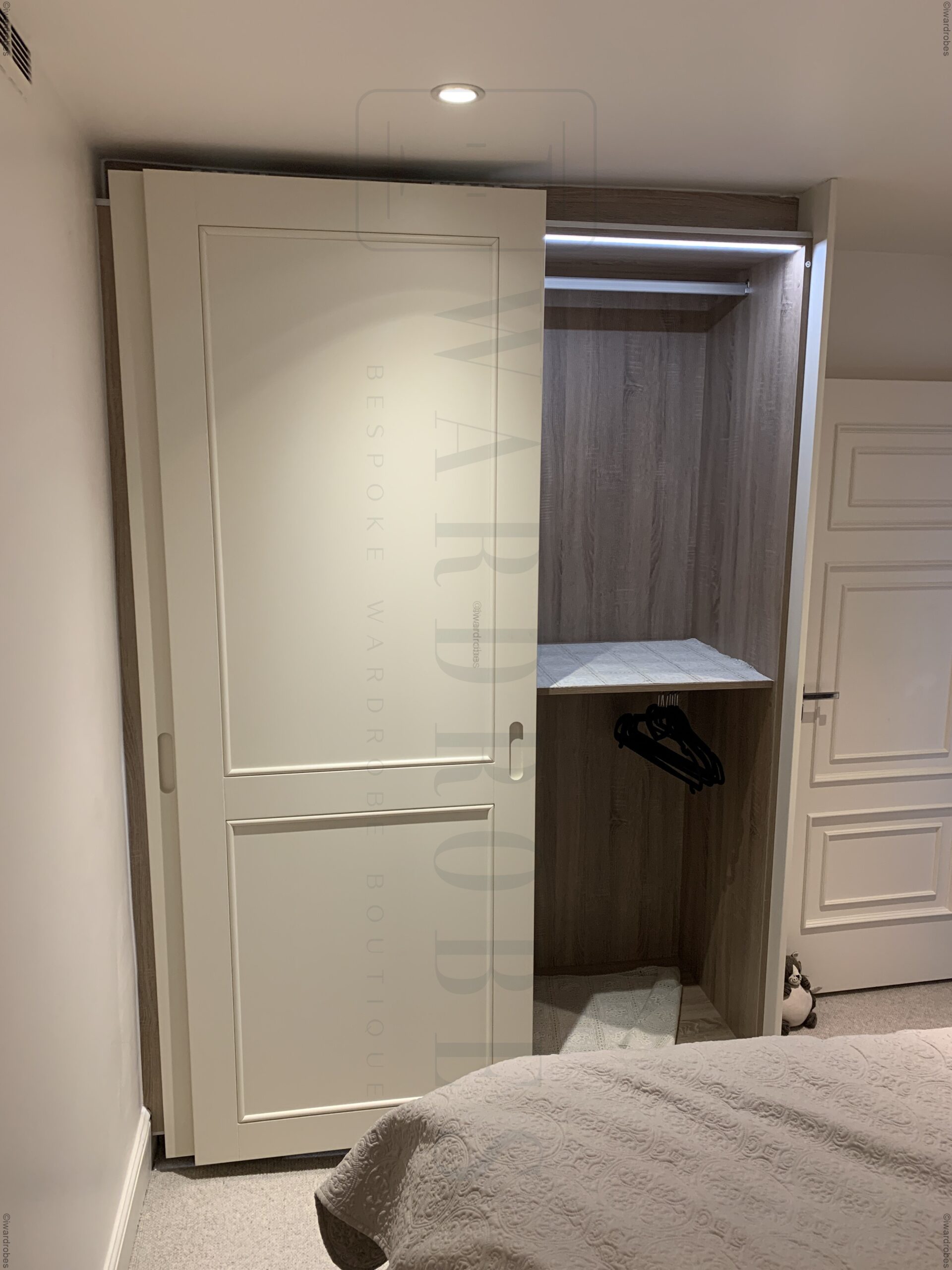 Bespoke sliding door shaker style wardrobe with open interior in bedroom.