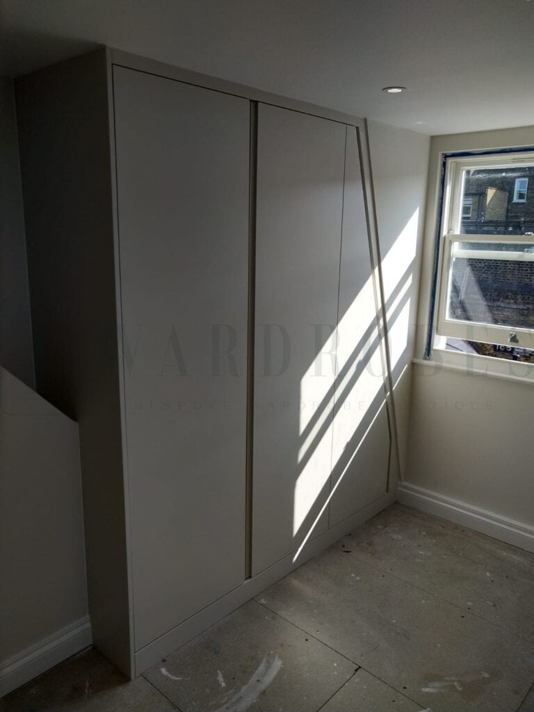 Modern white bespoke wardrobe with sloping ceiling in bedroom.