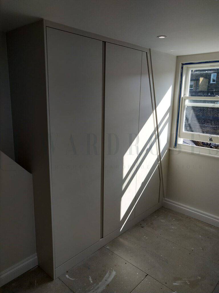 Modern white bespoke wardrobe with sloping ceiling in bedroom.