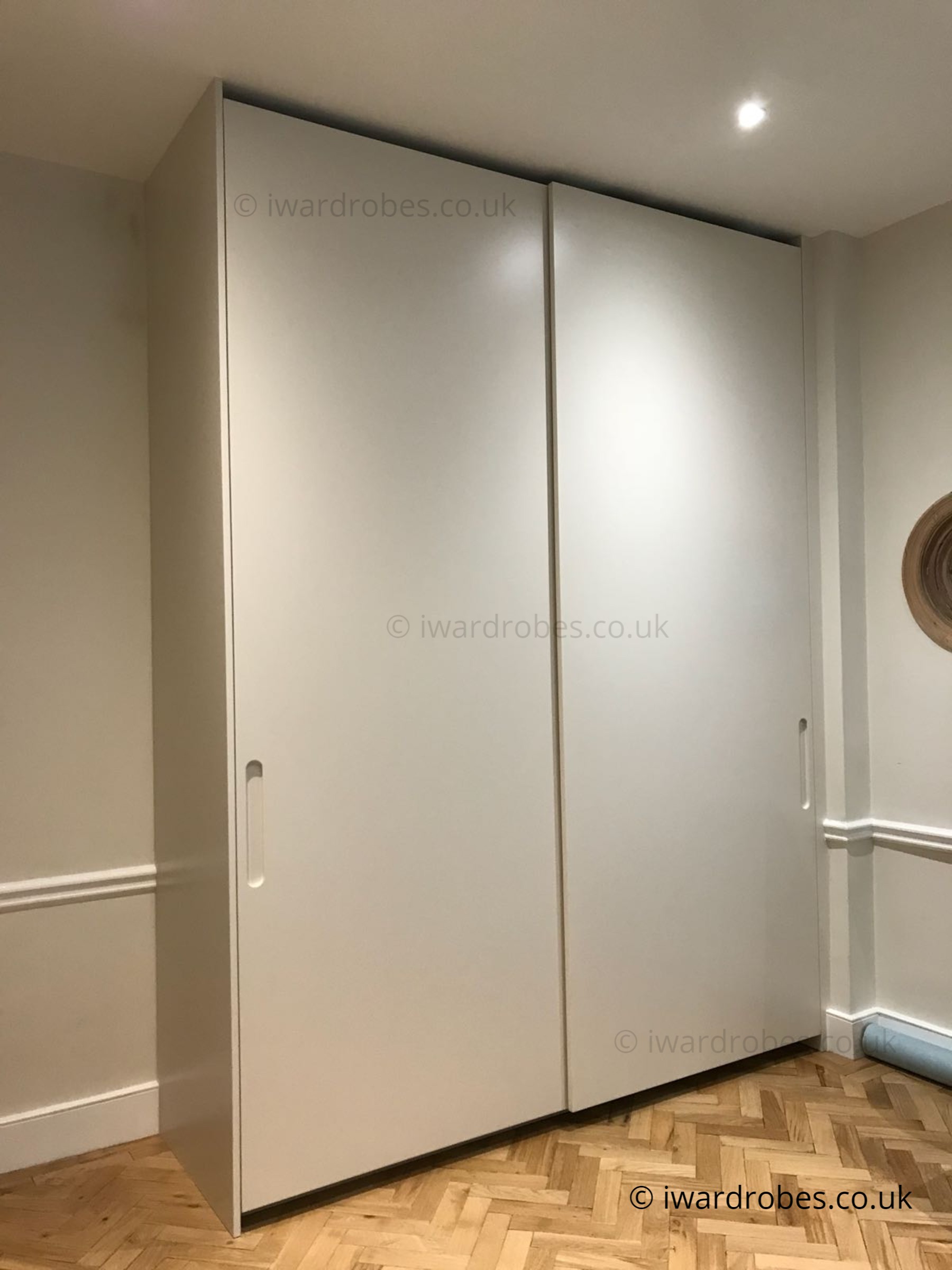 Modern white sliding door wardrobe with spray-painted finish in London home.